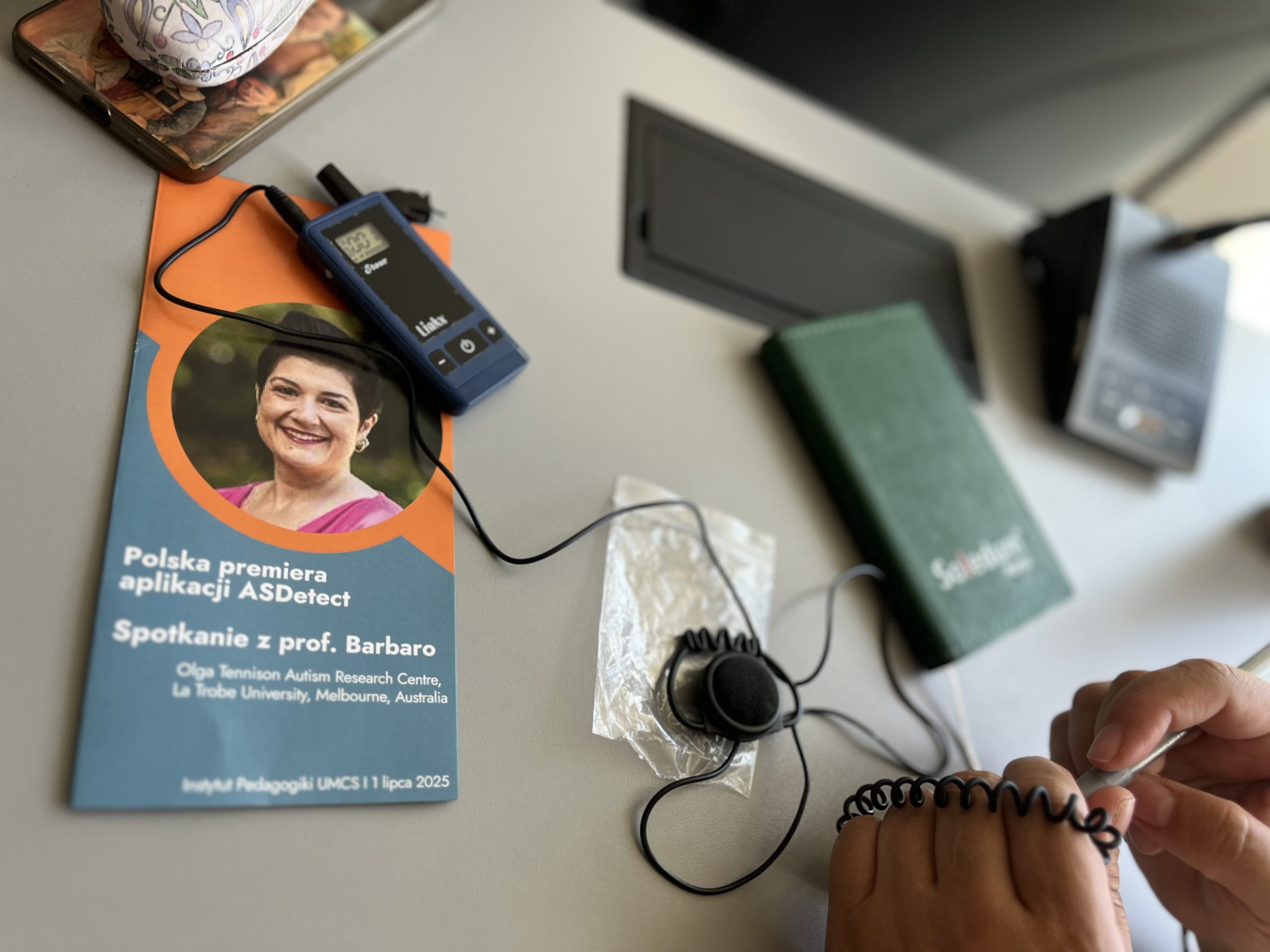 a desk with a brochure, hands, and an audio recording device