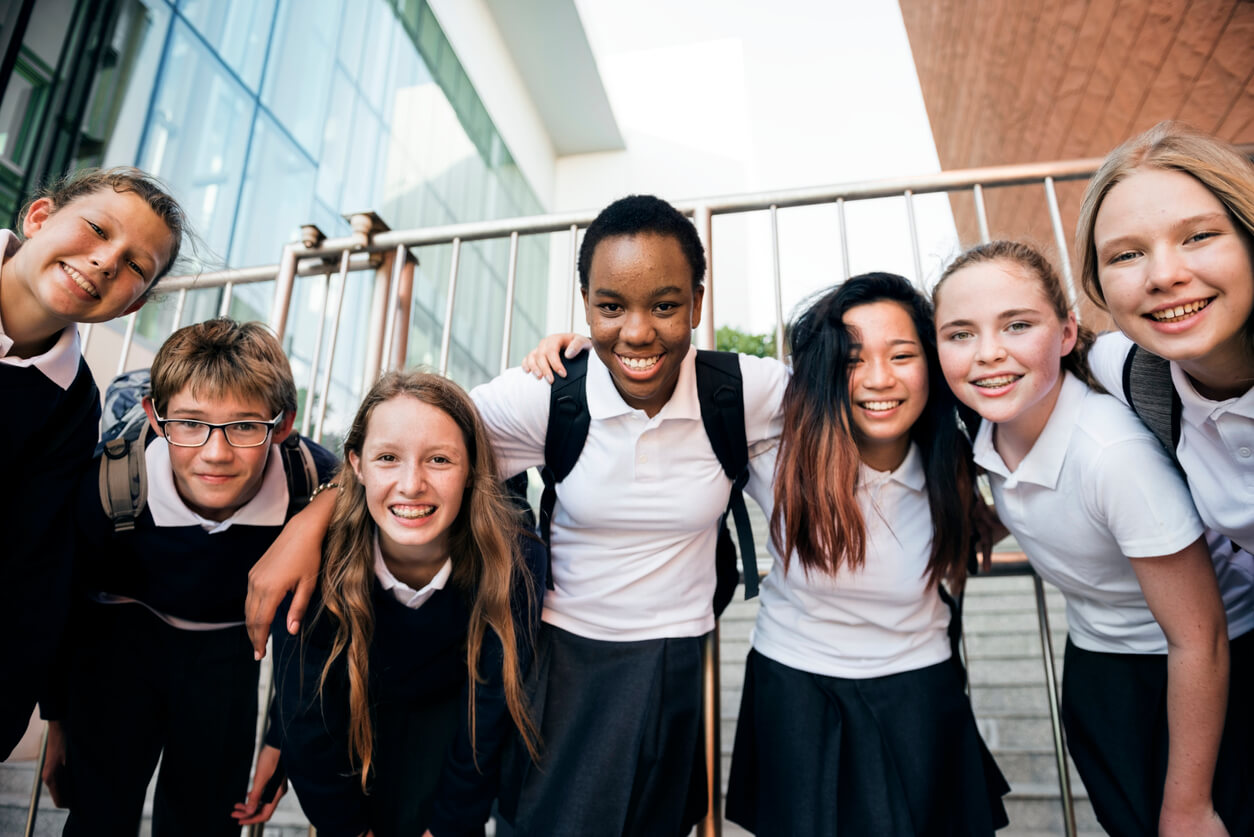 Several students in matching school uniforms gathered together, smiling and interacting in a schoolyard setting