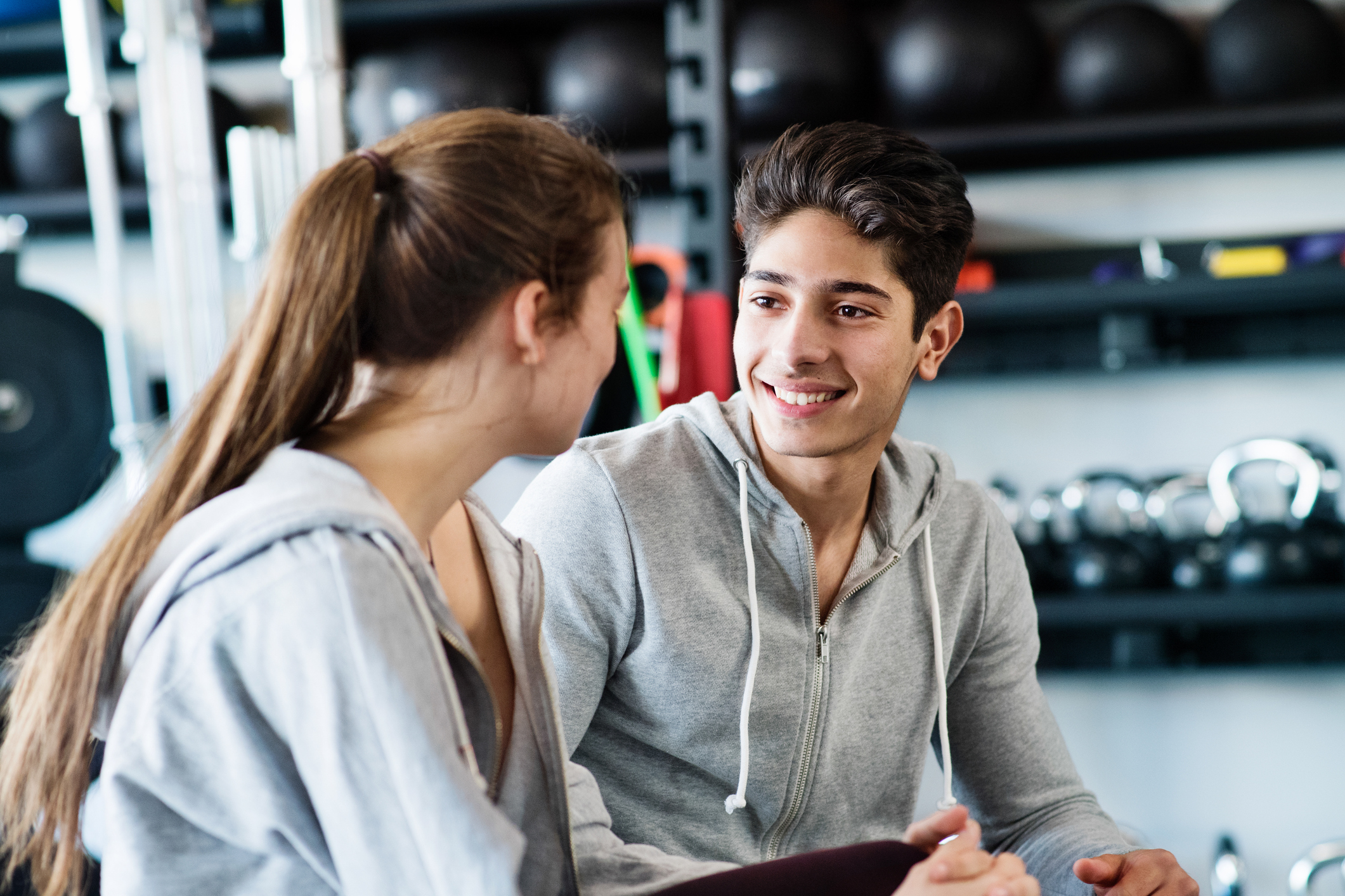 Two young people looking at each other in a gym setting, wearing grey workout clothing.