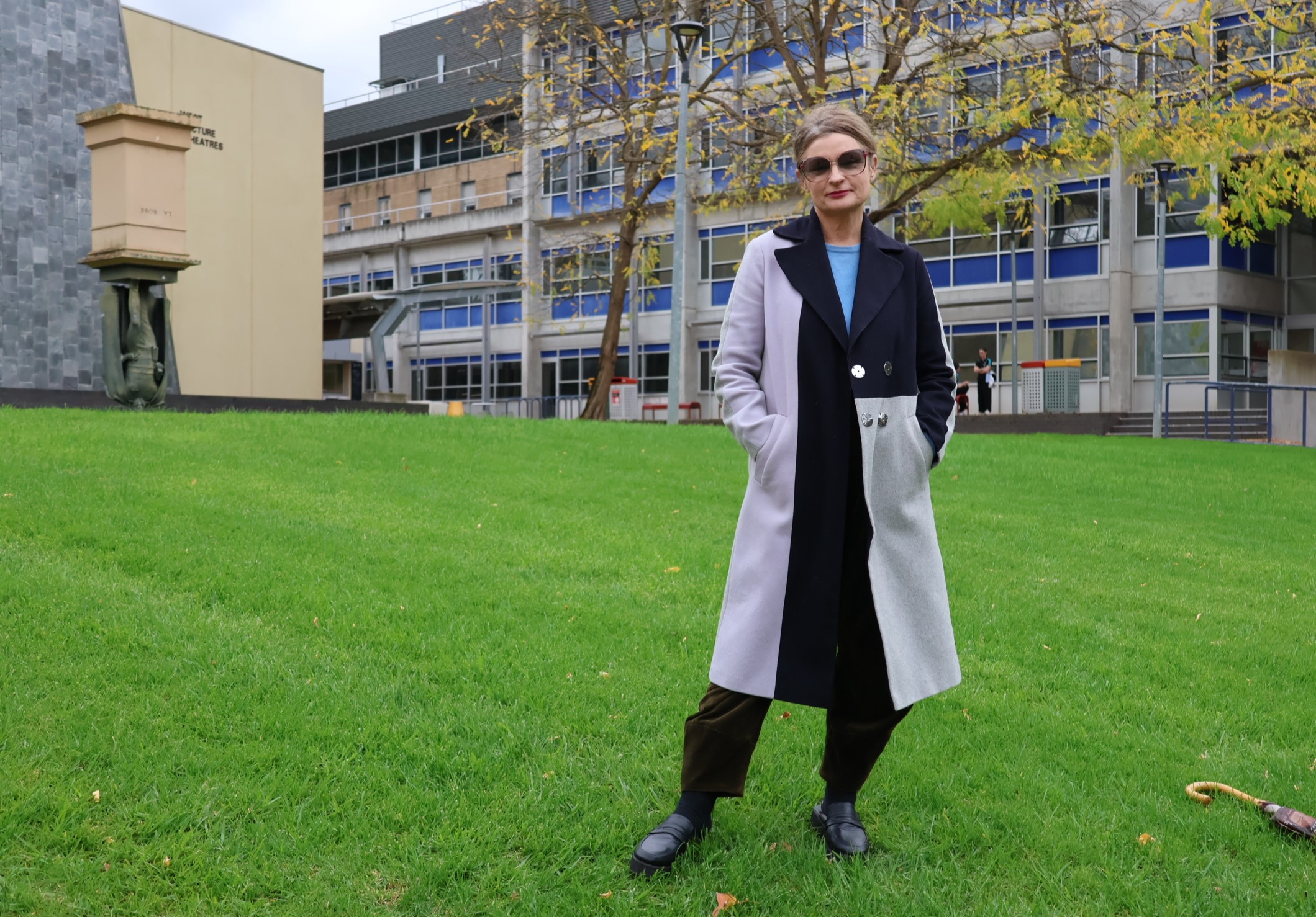 student standing on University lawn wearing sunglasses and a long block-patterned coat