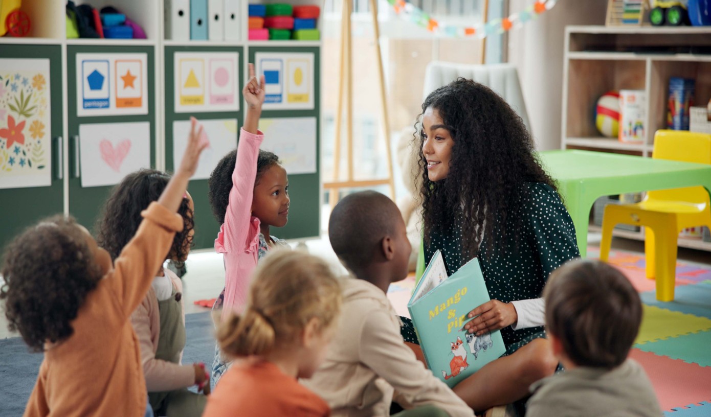 Early childhood educator reading a picture book to children in a colourful, engaging classroom environment.